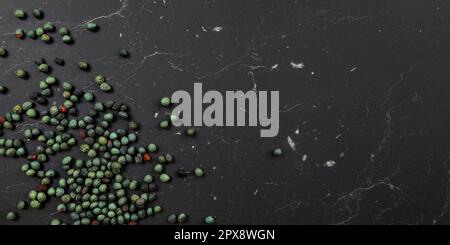 Tabletop view, Black pepper (Piper nigrum) spice spilled on dark marble like board. Turkish green / blue peppercorn variant. Banner with space for tex Stock Photo
