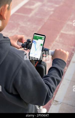 young man riding an electric skateboard outdoors, looking at route on smartphone map application, sustainable transport concept, zero CO2 emission gre Stock Photo