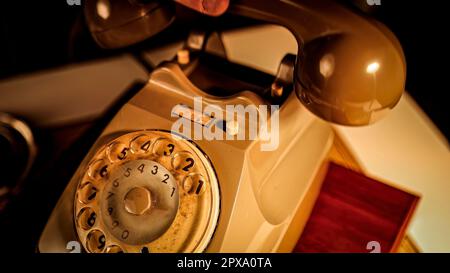 A man's hand picking up the receiver of an antique telephone placed on a table, lifting it up and off the hook. And then putting the receiver back ont Stock Photo