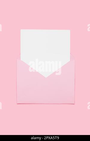 Closeup on blank empty white paper card in pink opened envelope isolated on pink pastel color background. Love letter minimal concept. Conceptual layo Stock Photo