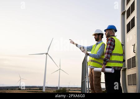 Team two young maintenance engineers working on wind turbine at wind farm. Copy space. Stock Photo