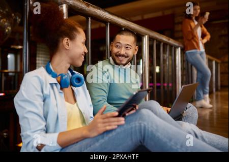 Diverse coworkers sitting on floor talking while using digital tablets in coworking office Stock Photo
