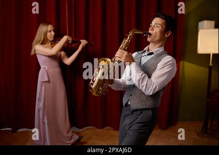 Sax man and woman fiddler duet playing classical melody. Musical duo jazz band on the stage in action Stock Photo