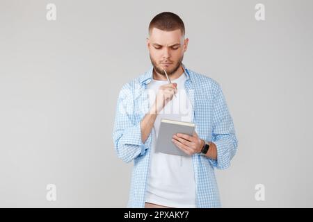 serious handsome man in casual blue shirt holding notebook, planning or thinking about question Stock Photo