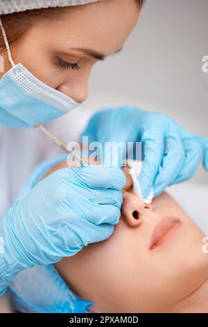 young woman during a mechanical face cleansing procedure at beauty clinic. Cosmetologist making procedure for cleaning skin with steel tool from black Stock Photo