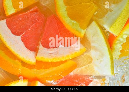 Slices of grapefruit, orange and pomelo in water on white background. Pieces of grapefruit, orange fruit and honey pomelo in liquid with bubbles. Slic Stock Photo