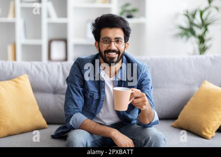 Handsome young indian guy relaxing on couch with cup of coffee Stock Photo