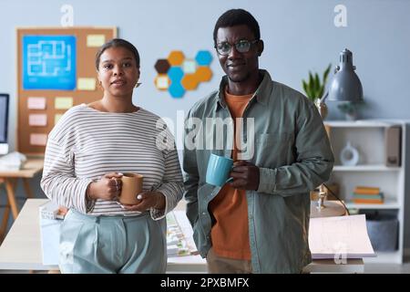 Portrait of couple of young engineers looking at camera while standing in office during coffee break Stock Photo