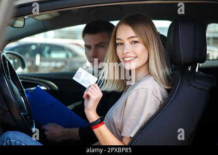 Joyful girl driving a training car with a drivers license card in her hands. Stock Photo