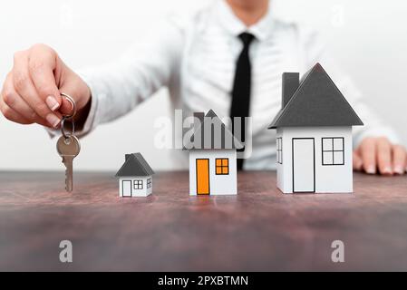 Businesswoman holding keys. olored paper houses standing on desk. Stock Photo