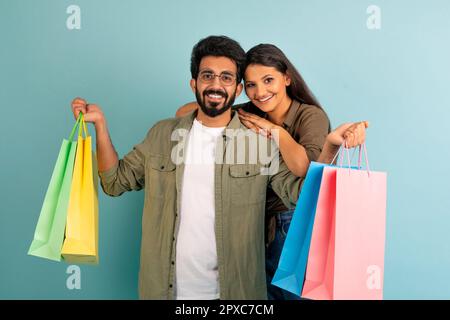 Beautiful indian couple posing with shopping bags on blue Stock Photo