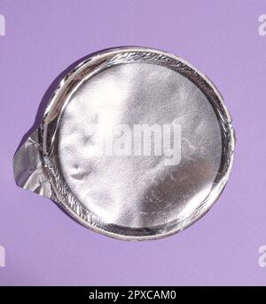 Aluminum round lid from under the package with chips on a purple background, flat lay Stock Photo