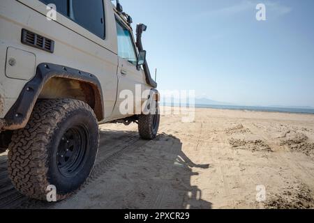 Off road vehicle parked on an empty sandy beach facing the sea. Stock Photo