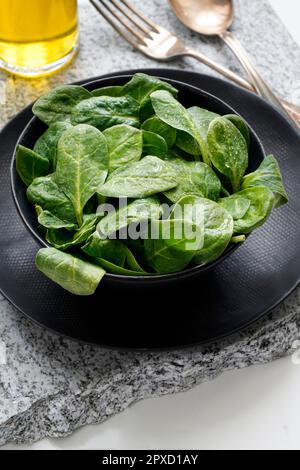 Fresh baby spinach in a black bowl and silver cutlery on a gray stone Stock Photo