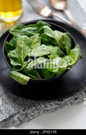 Fresh baby spinach in a black bowl and silver cutlery on a gray stone Stock Photo
