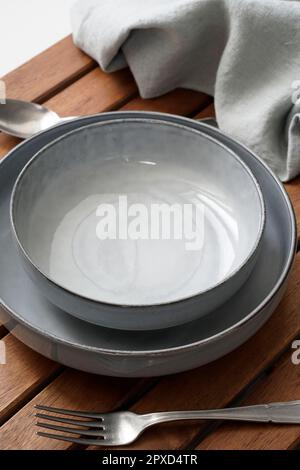Empty stoneware plates, silver cutlery and fabric on wooden background Stock Photo