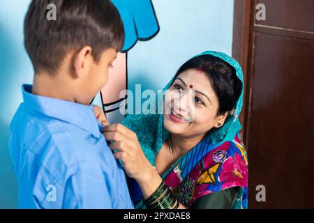 Young happy indian mother wearing sari getting her son ready for school. Education concept. Rural india. Stock Photo