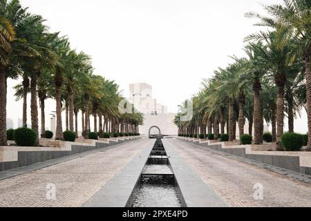 Doha, Qatar - April 2023, The iconic Museum of Islamic Art building designed by architect I.M. Pei is located on the Doha Corniche with palm tree rows Stock Photo