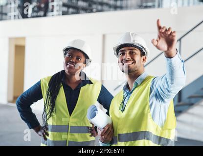 Were planning on adding more space here. two young contractors standing together in the warehouse and observing the layout. Stock Photo