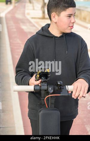 young teenager with a sideways glance riding an electric sscooter and using a smartphone application E-Mobility urban leisure concept Stock Photo