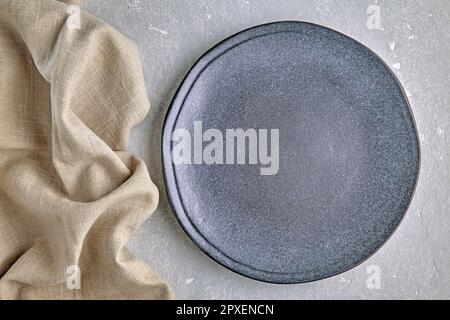 An empty gray ceramic plate and a rough linen napkin on a gray concrete table. Background for displaying food. Top view with copy space Stock Photo