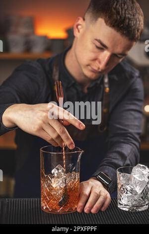 Young barman stirring fresh alcoholic cocktail with sweet fruit syrups on the bar counter Stock Photo