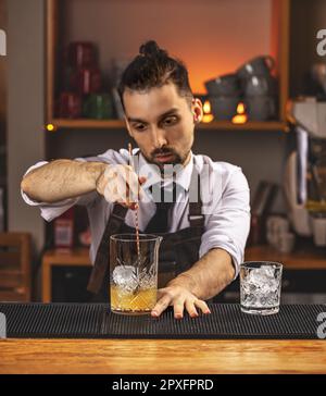 Young barman stirring fresh alcoholic cocktail with sweet fruit syrup on the bar counter Stock Photo