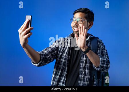 Happy student, college male student, smiley face, making video call, blue background. One university student doing video call on phone. Stock Photo