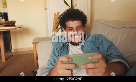 Happy guy holds smartphone in his hands, sends text message, communicates in social networks, surfs the web while sitting indoors Stock Photo