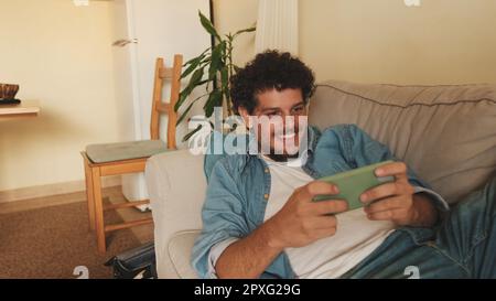 Happy guy holds smartphone in his hands, sends text message, communicates in social networks, surfs the web while sitting indoors Stock Photo