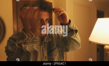 Close-up of an unshaven guy looking at himself in the mirror, touching his chin and head Stock Photo