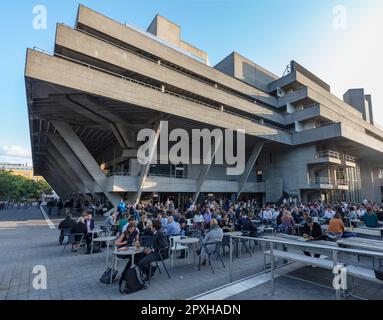 People at cafe, bar, restaurant outside the National theatre brutalist style building by Denys Lasdun in the South Bank Complex opened in 1976. London Stock Photo