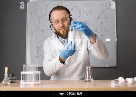 Online remote learning. Teacher with chemical flask showing experiments having video conference chat with student and class group. Teaching and Stock Photo