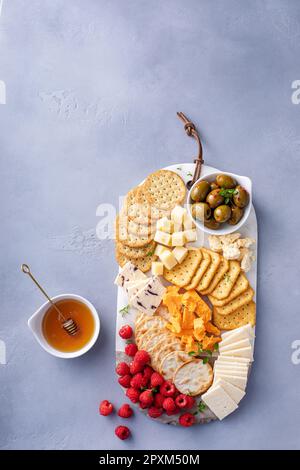 Cheese board or snack board with crackers, cheese, olives and raspberries Stock Photo