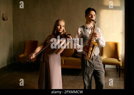 Young female violinist and male saxophonist training at home studio before music concert performance Stock Photo