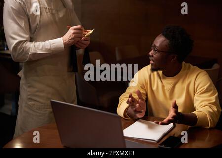 African American young man discussing menu with waiter while he making notes during lunch in cafe Stock Photo
