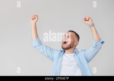 amazed young man celebrating victory on gray background. Stock Photo