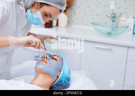 beautician applies blue alginate mask to the face of beautiful woman in the spa salon. spa treatments Stock Photo
