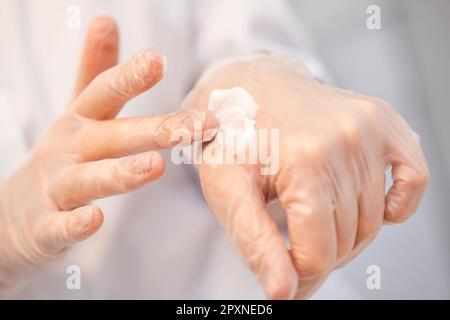 beautician in gloves applies cream on his hand and shows the texture of the cream Stock Photo