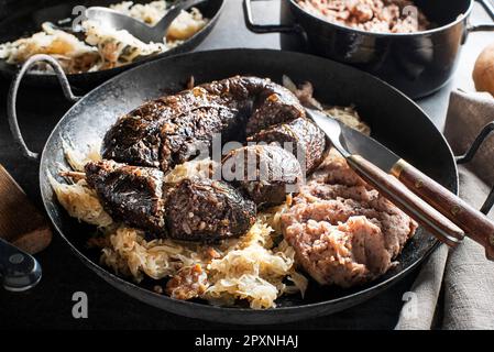 Bloody sausage morcilla, stewed sauerkraut and mashed potato with beans close up. Traditional Slovenian dish with roasted bloody sausage Stock Photo