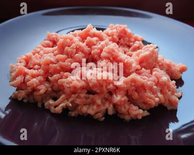 Minced meat on a purple ceramic large plate. Delicious fresh ground meat for making cutlets, steaks, hamburgers, meatballs. Pork semi-finished product Stock Photo