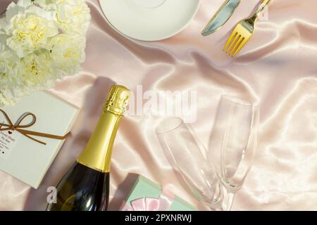 Festive table set concept, Champagne with glass and peony with gift box on table cloth for diner. Stock Photo