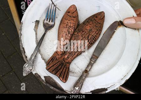 Wooden fish, metal fork and knife on a weathered plate outside a restaurant Stock Photo