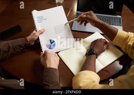 High angle view of colleagues discussing financial report while sitting at table with laptop during meeting in cafe Stock Photo