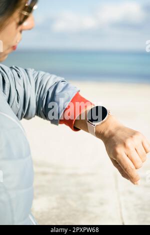 Cropped photo of a stylish woman checks notification on wearable digital wrist watch monitors the weather wears casual jacket poses on the street. Wom Stock Photo
