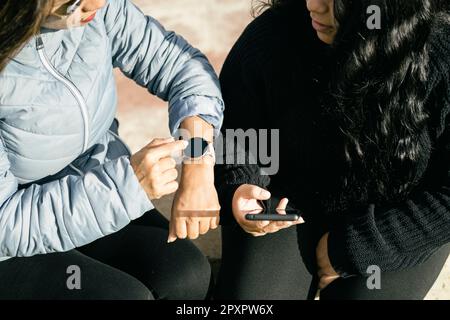 Two young beautiful female friends with smart devices texting and chatting having fun on social media, smart phone r and smart watch smart technology Stock Photo