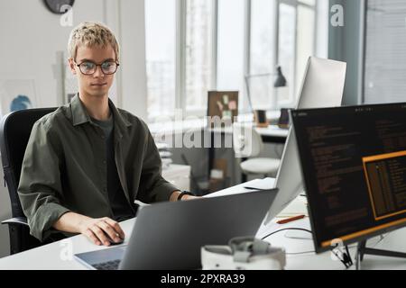 Young programmer in eyeglasses concentrating on his work with codes for new software while sitting at his workplace in office Stock Photo