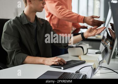 Close-up of two programmers pointing at monitor and discussing presentation on computer while working at table in team Stock Photo