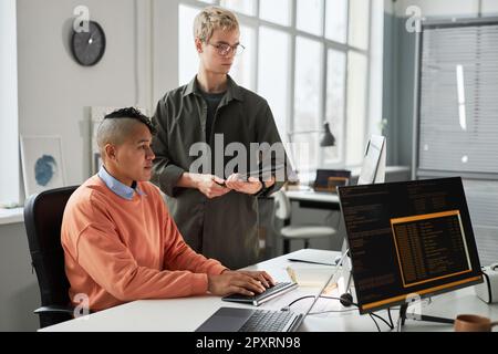 Colleagues working over computer program in team, they sitting at table and typing computer codes on computer Stock Photo