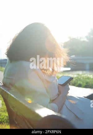 unrecognizable young woman reading his smartphone on urban bench Stock Photo